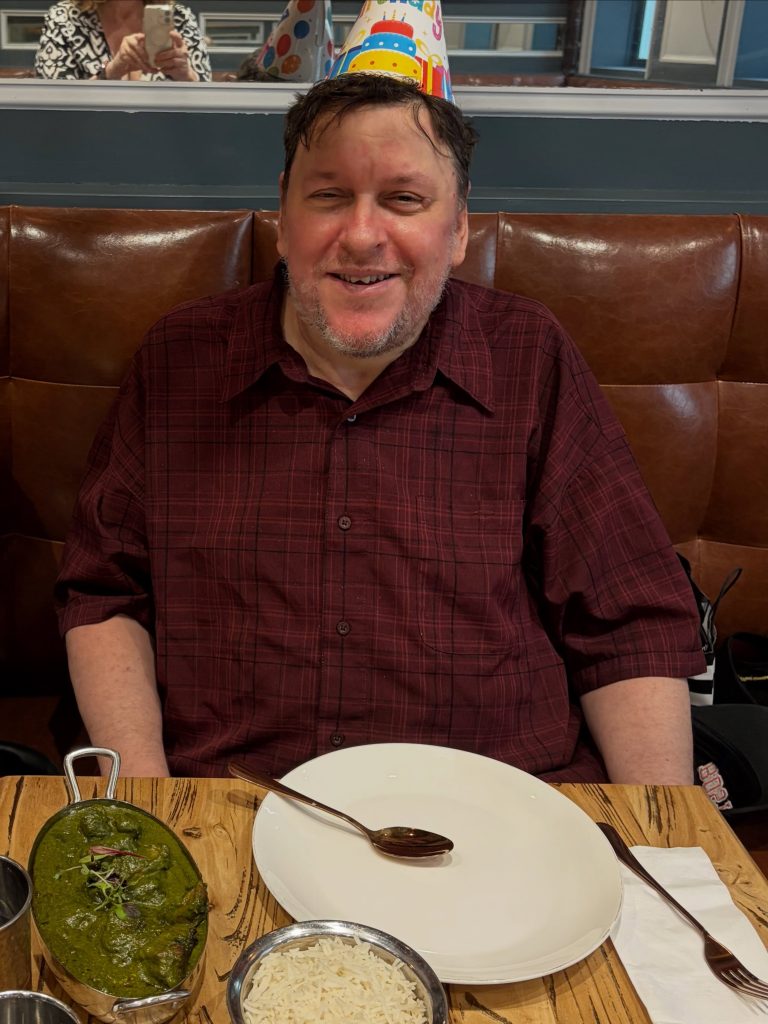 A member smiling in a party hat at a birthday lunch