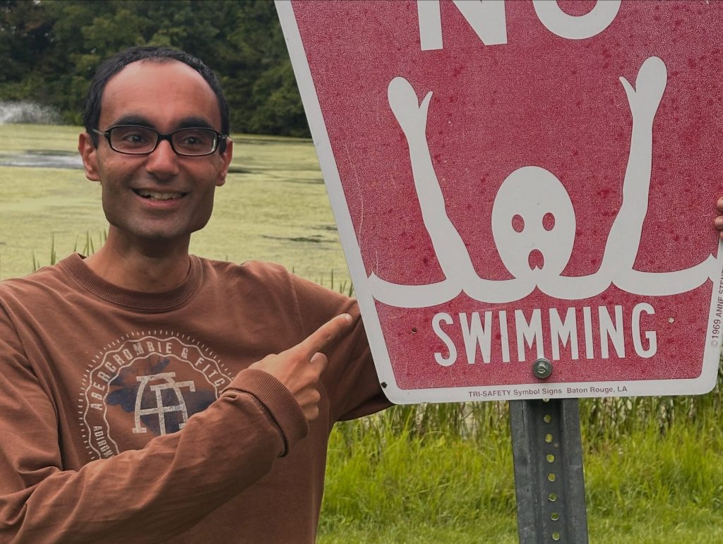 A member grinning and pointing at a No Swimming sign at Leonard Park