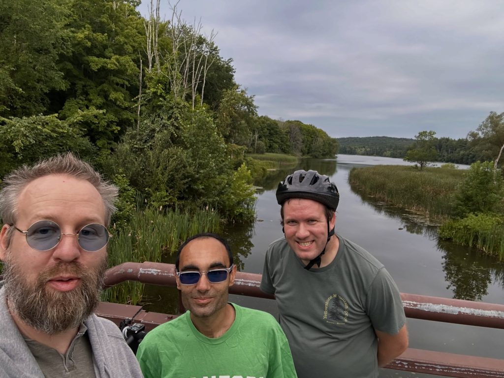 Three members taking a selfie on a bridge during an e-bike trip along a Westchester reservoir